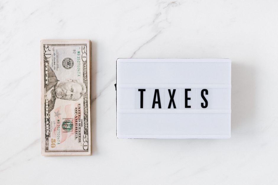 Top view composition of stack of American dollars placed on white marble surface with white retro light box with TAXES inscription