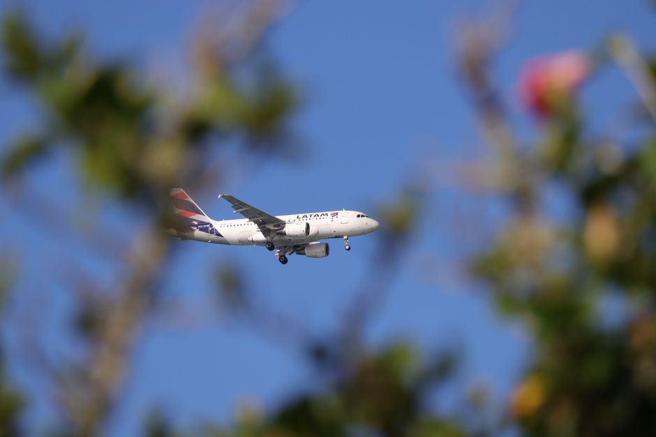 LATAM airplane captured mid-flight over a vibrant blue sky in Florianópolis, Brazil.