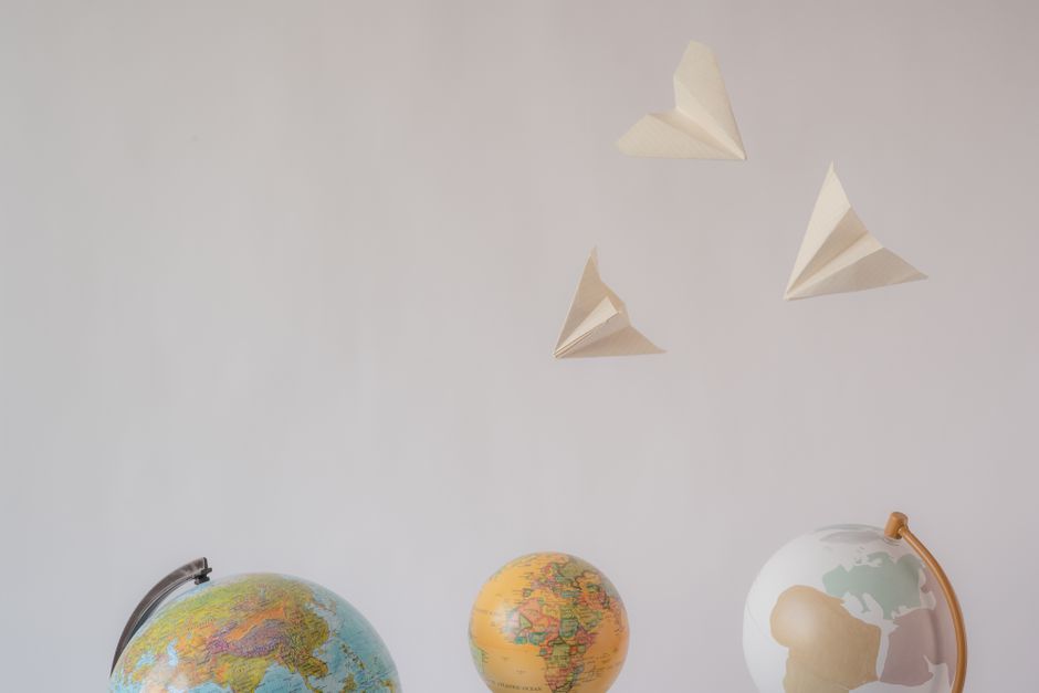 Paper airplanes fly over colorful globes, symbolizing travel and exploration on a white background.